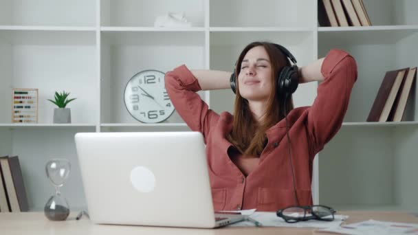 Leende nöjd ung affärskvinna klar dator arbete stretching sitter vid arbetsplatsen skrivbord. Glad avslappnad affärskvinna lyssnar på hörlurar känna stress lättnad efter väl utfört arbete — Stockvideo