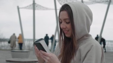 Parkta telefonda oyun oynayan neşeli kız. Akıllı telefon kullanan oyuncu kadın.