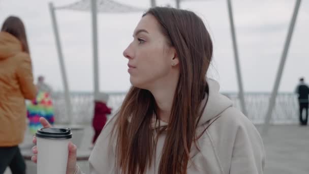 Italok és emberek koncepció - boldog fiatal nő vagy tizenéves lány iszik kávét papírpohárból ül a városi utcai padon — Stock videók