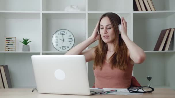 Glimlachend tevreden jonge zakenvrouw klaar met computerwerk stretching zitten aan het bureau van de werkplek. Gelukkig ontspannen zakenvrouw luisteren naar koptelefoon gevoel stress verlichting na het werk goed gedaan — Stockvideo