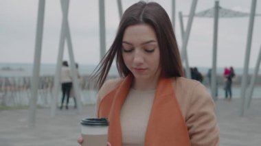 İçkiler ve insanlar konsepti - mutlu genç kadın ya da genç kız şehir bankında oturmuş kağıt bardaktan kahve içiyor.