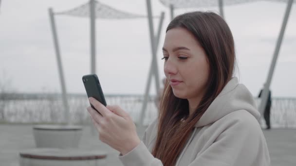 Tevreden aantrekkelijke brunette meisje types sms-bericht op mobiele telefoon, geniet van online communicatie, types feedback. Technologieconcept — Stockvideo