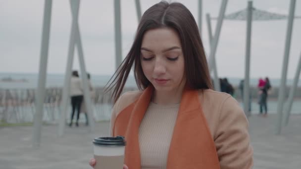 Drankjes en mensen concept - gelukkige jonge vrouw of tienermeisje het drinken van koffie uit papieren beker zittend op de stadsbank — Stockvideo