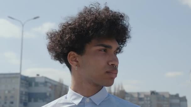 Primer plano joven divertido hombre africano pelo rizado de 20 años de edad lleva camisa blanca azul posando mirando cámara encantadora sonrisa de pie en la calle. Gente emociones sinceras concepto de estilo de vida — Vídeos de Stock