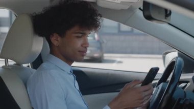 Afro-Amerikalı öğrenci akıllı telefon kullanıyor, arabada oturuyor, sosyal ağlarla iletişim kuruyor, erkek alet kullanıcısı. Mesaj yazan genç adam.