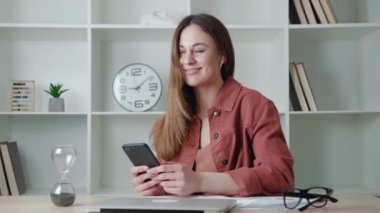 Güzel genç bir kadın cep telefonu kullanarak kablosuz kulaklıkla müzik dinliyor.