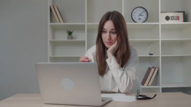 Modern bir ofiste çalışan genç ve ciddi bir kız dizüstü bilgisayarında daktilo ediyor ve bir not defteri yazıyor.