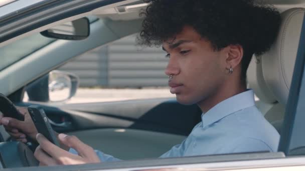 Крупным планом молодой афроамериканец едет в машине и звонит на смартфон. Красивый счастливый мужчина говорит по мобильному телефону, сидя в современном автомобиле. Автомобильная концепция — стоковое видео