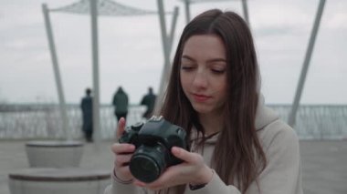 Elinde fotoğraf makinesi olan ve bir objeye odaklanan genç bir kadın gülümsüyor ve parkta fotoğraf çekiyor.