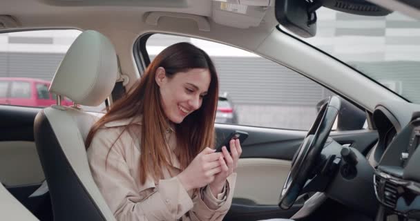 Una mujer joven se sorprende, desconcertada por lo que vio en un teléfono inteligente. Mujer sentada en coche. — Vídeo de stock