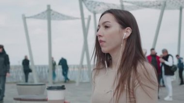 Kulaklıklı, mutlu genç bir kadının şehirde tek başına eğlenmesi. Neşeli, çekici, esmer, kaygısız kadın müzik dinliyor ve kahve içiyor.