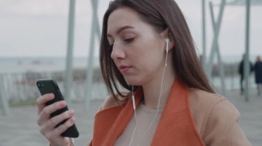 Kulaklıkla müzik dinleyen çekici genç bir kadın. Şehirde akıllı telefon kullanıyor. Etrafına bak.