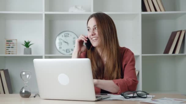 Бізнес-леді розмовляє по телефону під час використання ноутбука — стокове відео