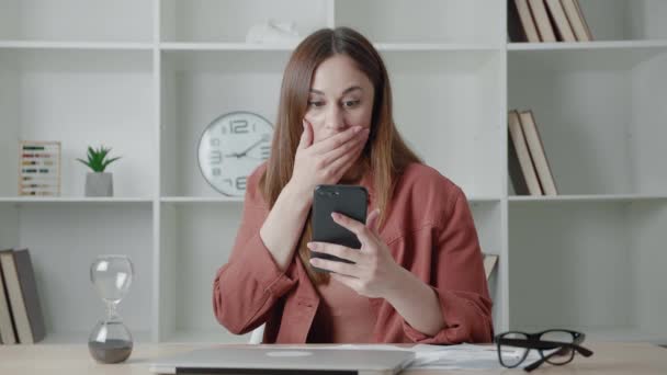 幸せなビジネス女性はよいニュースを読むsmsメッセージを受け取る。自宅のオフィスのデスクに座っているスマートフォンを見て成功を祝う興奮した男性の勝者。モバイル勝利コンセプト — ストック動画