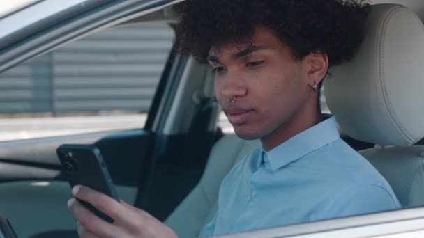 Çekici afro-amerikan genç işadamı araba tebessümünde telefonla konuşuyor direksiyonda oturuyor genç araç açık yolcu koltuğu otomobil sokağı otomobil işadamı ceketi satın alıyor yavaş çekimde yakın çekim — Stok video