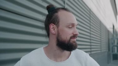 Kameraya bakıp gülümseyen sakallı, neşeli bir hippi erkek. Modern kabarık şirket ofisinin yakınında yakışıklı beyaz bir adam. Portreler. İnsanlar ve duygular kavramı