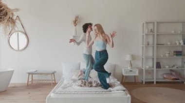 Mutlu, genç çift yatakta dans ediyor. Kaygısız hipster ve genç sarışın. Sabahları evdeki rahat yatak odasında eğleniyorlar.