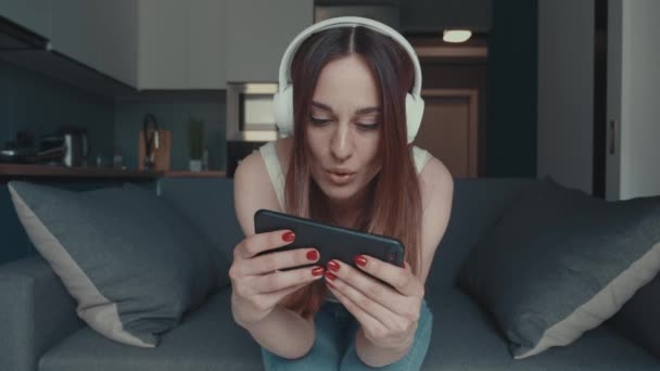 Bonne femme gamer porter casque compétition jouer à un jeu vidéo en ligne avec smartphone dans le salon à la maison. Esport streaming jeu en ligne, concept d'activité de quarantaine à domicile. — Video