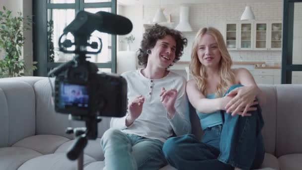 Happy couple bloggers filming new vlog video with the professional camera at home. Content millennial creators sitting on sofa and filming live vlog. Vlogger recording vlog with video camera — Stock Video