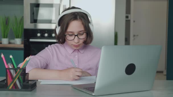 Gülümseyen zeki liseli kız öğrenci, evde ders çalışıyor. Masasında oturmuş bilgisayarına bakıyor. Mutlu şirin ilkokul öğrencisi egzersiz kitabına yazıyor ödev yapıyor, masada öğreniyor.. — Stok video