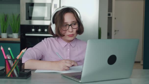 Lachende tiener Kaukasisch meisje in hoofdtelefoon heeft videogesprek verre klasse met leraar met behulp van laptop, gelukkige school kind praten met tutor, online studeren op de computer. Thuisonderwijs, afstandsonderwijs, e-learning — Stockvideo