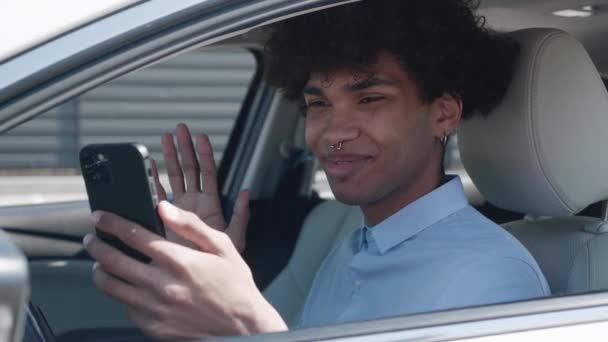 Feliz joven afroamericano con estilo hablar videochat en el teléfono inteligente sonriendo sentado en el coche. Divertido empresario de comunicación. — Vídeo de stock