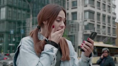 Kazanan kot ceketli genç bayan akıllı telefon ekranına bakıyor ve iyi haber zaferini kutluyor. Şehir arkaplanı
