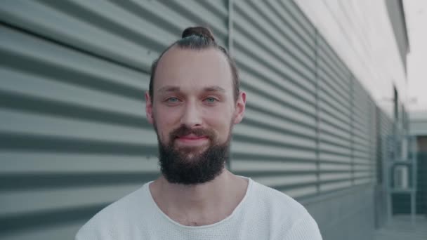 Nahaufnahme des Millennial-Mannes, der in die Kamera schaut und lächelt. Porträt eines gutaussehenden Typen mit Bart, der an der Straße steht. Konzept von Menschen und dem realen Leben. — Stockvideo