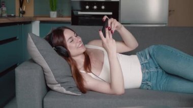 Çekici bir kadın evdeki oturma odasında rahat bir kanepede uzanıp akıllı telefonuyla online video oyunları oynuyor. Sevimli genç kız evde Coronavirus kilitleme durumuyla uğraşırken oyun oynamaktan hoşlanıyor.