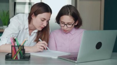 Ciddi bir kız, masada bilgisayarın önünde annesinin yanında ödev yapıyor. Genç bir anne evdeki görevlerde çocuğa yardım ediyor. Gözlüklü genç kız içeride ebeveyn desteğiyle uzaktan eğitim görüyor.