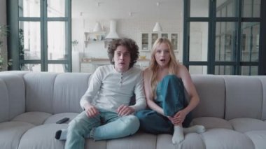 Neşeli çift futbol fanatikleri maç desteği izliyorlar futbol takımını kazanan takım kanepede birlikte oturuyorlar, mutlu milenyumlar zaferi kutluyorlar gol skoru televizyon maçı