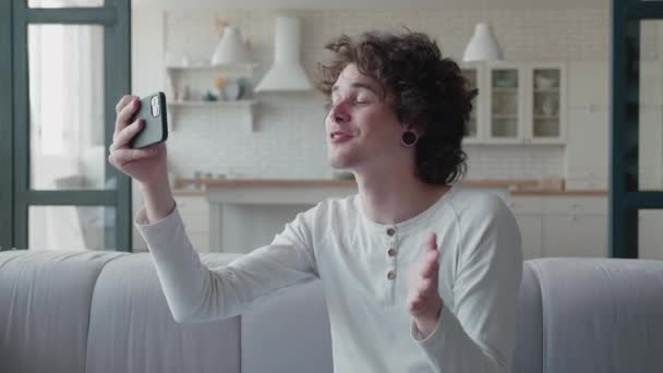 Video de un joven guapo haciendo videollamada desde casa saludando con la mano — Vídeo de stock