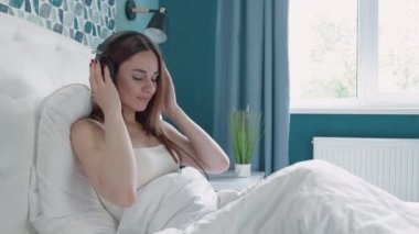 Güzel, genç bir kadın, mutlu kulaklık takıyor, dinleniyor, dinleniyor, yatak odasında dinleniyor, kadın eğlencesi ve akıllı cep telefonunda şarkı çalan kulaklık, yaşam tarzı kavramı..