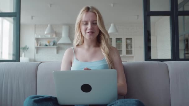 Ung glad blond vlogger kvinna viftar hand tittar på webbkamera håller laptop sitter på mysig soffa videokonferens ringer i virtuell chatt möte med sociala avstånd vän. — Stockvideo