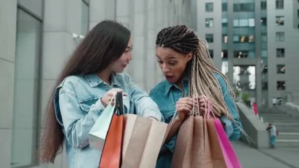 Duas amigas com sacos multicoloridos. duas jovens após as compras compartilham suas impressões. Amigos se conheceram em uma venda — Vídeo de Stock