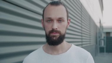 Gülümseyen sakallı milenyum hippisi mavi gözlü kameraya bakıyor. Mutlu, kendine güvenen, zeki, genç, yetişkin bir lider. Milenyum pozu, şehrin arka planında. Yüz görünümlü erkek portresini kapat