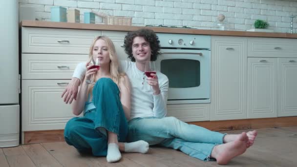 Счастливая молодая пара подростков, сидящая на теплом подогреваемом полу. звон бокалов с вином, празднование праздника, романтическое свидание в арендованных апартаментах — стоковое видео