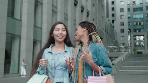 Két gyönyörű ázsiai és afrikai lányok szórakozás séta az utcán a vásárlások vásárlás után, Steadicam lövés — Stock videók