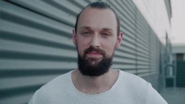 Gülümseyen sakallı milenyum hippisi mavi gözlü kameraya bakıyor. Mutlu, kendine güvenen, zeki, genç, yetişkin bir lider. Milenyum pozu, şehrin arka planında. Yüz görünümlü erkek portresini kapat
