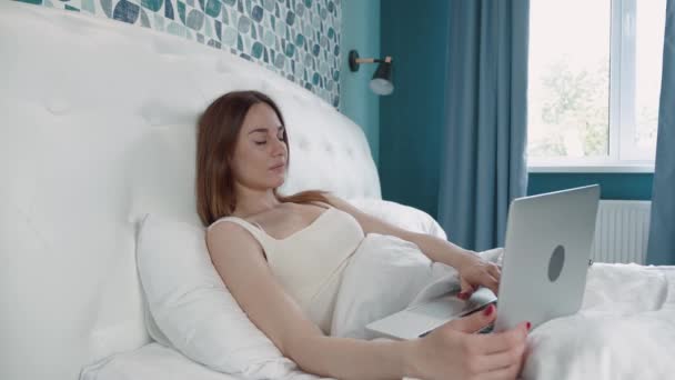 Jeune femme de travail ordinateur portable sur le lit. Jolie jolie femme travaillant de la maison sur ordinateur portable clé de la chambre. — Video