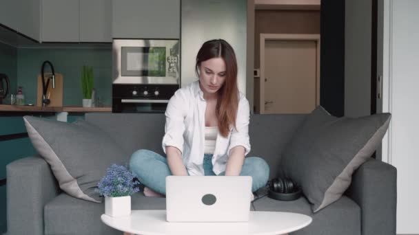 Młoda studentka, młoda kobieta pracownik zdalny za pomocą laptopa pracy studiuje online z biura w domu siedzieć na kanapie robi freelance odległość pracy w słonecznym przytulne mieszkanie. — Wideo stockowe