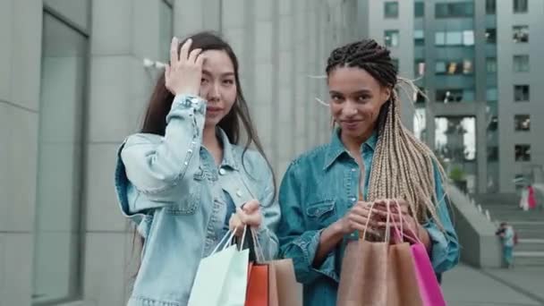 Amigos retrato con dos mujeres jóvenes felices sonriendo con bolsas de compras después de comprar ropa en la tienda de moda — Vídeos de Stock