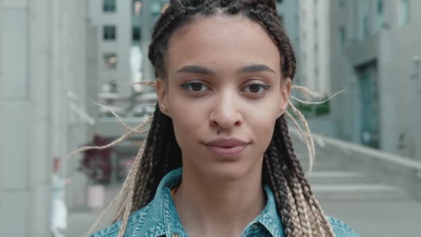 Close up retrato de jovem bela mulher afro-americana em uma jaqueta de ganga com dreadlocks de pé olhando para a câmera sorrindo sobre o fundo do centro de negócios — Vídeo de Stock