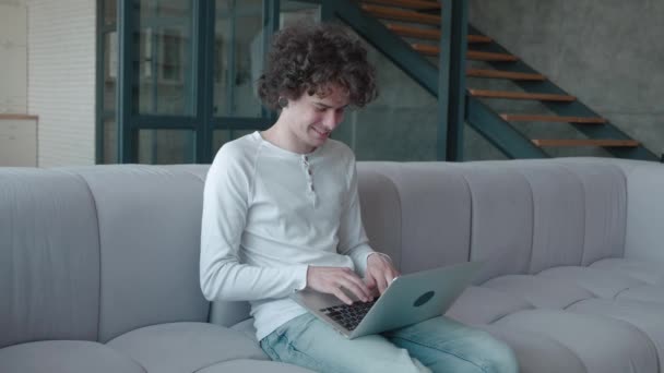 Aangename jonge millennial hipster guy met piercings typen bericht op computer zitten gezellige bank in modern interieur — Stockvideo