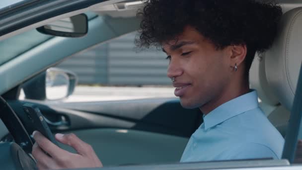 Afro-amerykański student używa smartfona, siedzi w samochodzie, komunikuje się w sieciach społecznościowych, męski użytkownik gadżetu. Młody facet pisze wiadomość — Wideo stockowe