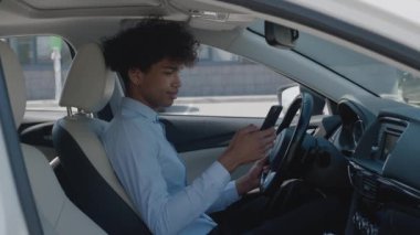 Yakın plan Afro-Amerikan adam. Arabadan telefona bakıyor. İyi giyimli adam arabada akıllı telefondan konuşuyor.