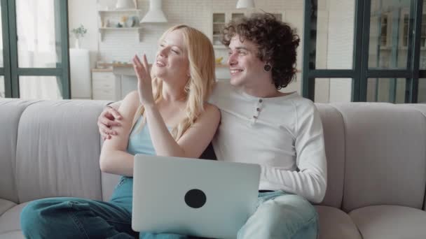 Junges Paar auf dem Sofa schaut sich etwas im Laptop an und träumt von der Renovierung des Hauses — Stockvideo