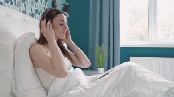 Selbstbewusste junge Frau liegt glücklich Kopfhörer Musik hören mit entspannen und genießen im Schlafzimmer, weiblichen Spaß und entspannen Kopfhörer mit Abspielen von Songs auf dem Smartphone, Lifestyle-Konzept. — Stockvideo
