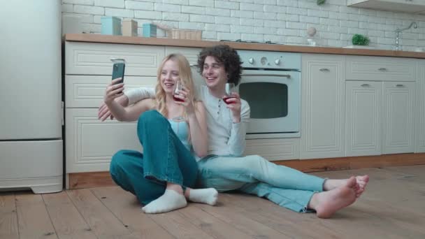 Молодая пара делает селфи, сидя на полу кухонного фона — стоковое видео