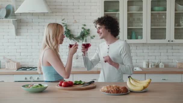 Pareja joven comiendo ensalada y fruta beber vino tinto en la cocina — Vídeos de Stock